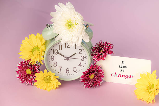istock Time for a change message on a tag.  Retro alarm clock surrounded by fresh flowers on a pink background. 2244966296