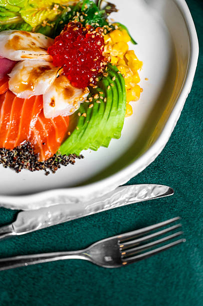A gourmet poke bowl with fresh sliced salmon, avocado, corn, and bright red salmon roe, elegantly plated on a white dish against a dark green background