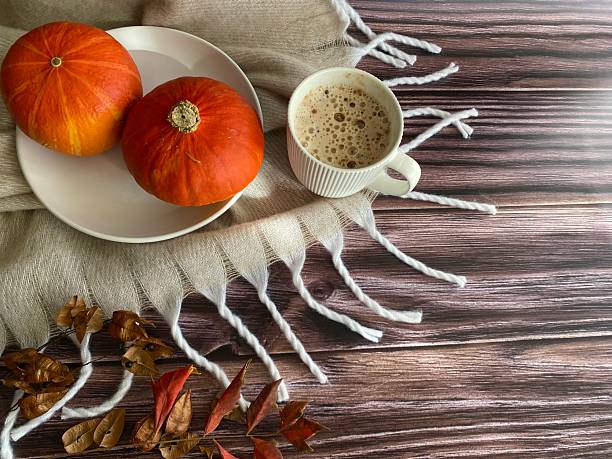 istock Cozy autumn composition with a warm beige blanket, two small orange pumpkins, fall leaves, and a cup of latte on wooden background 2244973218
