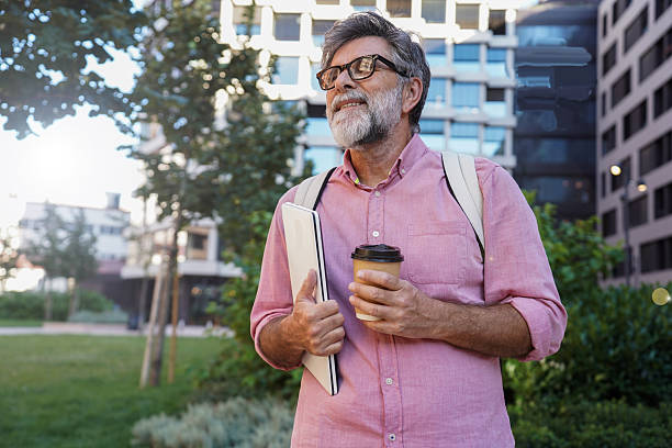 istock Older man drinking takeaway coffee while holding laptop in a modern setting 2244973648