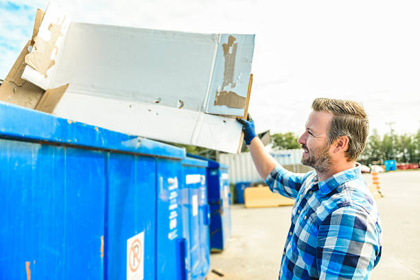 Recycling. Smiling man holding cardboard box with different waste paper on light background
