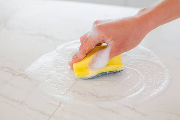 istock Hand scrubbing a white marble countertop with a yellow sponge and bubbly soap, ensuring a clean and hygienic surface 2244976992