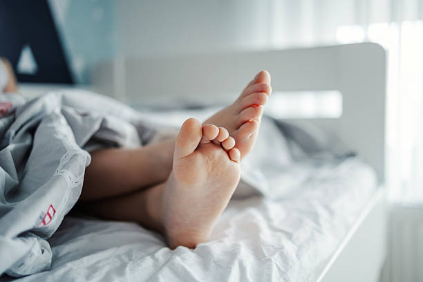 Child's feet sticking out from under a duvet, resting comfortably in bed. Representing sleep, relaxation, and a cozy morning