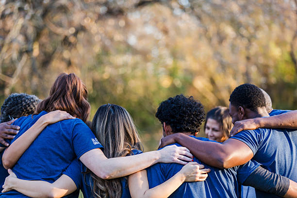 istock Diverse group of people in blue shirts hugging outdoors, showing unity and teamwork. 2244985471