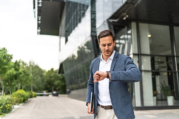 istock Young businessman checking time on watch with modern building 2244986224