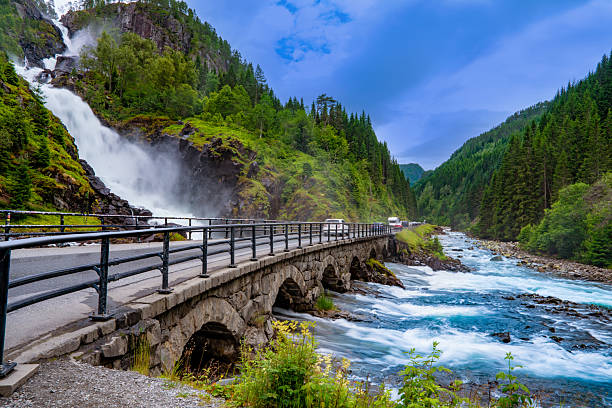 Powerful Latefossen waterfall behind stone arch bridge in Hardanger Norway on bright summer day.