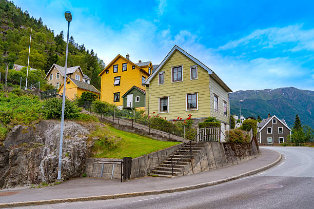 Colorful hillside houses in Odda residential street with mountain backdrop and blue summer sky in Norway.