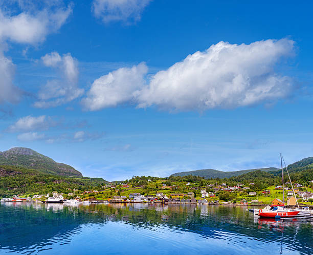 Red sailboat moored in Herand harbor on calm Hardangerfjord fjord with village and green mountains in Norway.