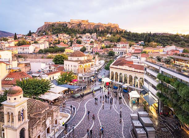 People walking in the square in the foreground, with the Ancient Greek Parthenon on The Acropolis on the horizon.