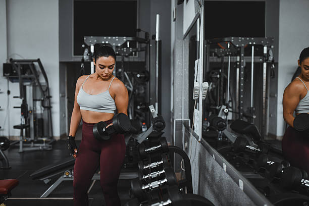 istock Female Gym Athlete Lifting Dumbbell During Group Training With Male Instructor Overlooking 2244991900
