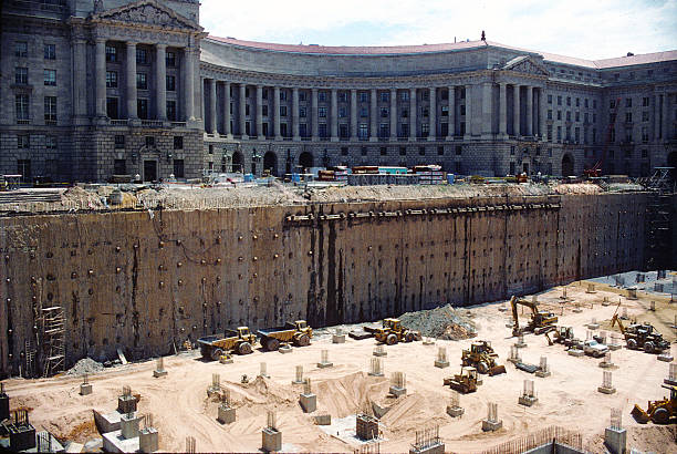 Large high-rise under construction in a metropolitan skyline with cranes and extensive scaffolding, partially covered facade against a clear blue sky signaling urban growth