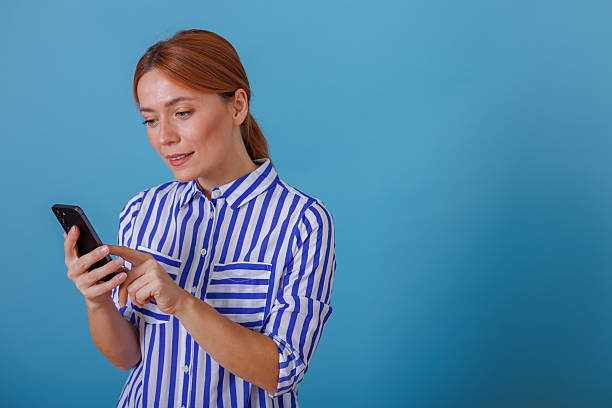 istock Woman scrolling smartphone, engaging with social media on a blue background, representing communication and online activity 2244996147