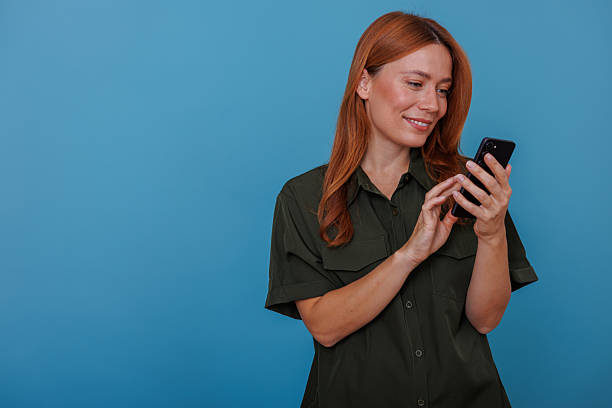 istock Woman standing against a blue background, happily interacting with her smartphone for communication and online activity 2244996422