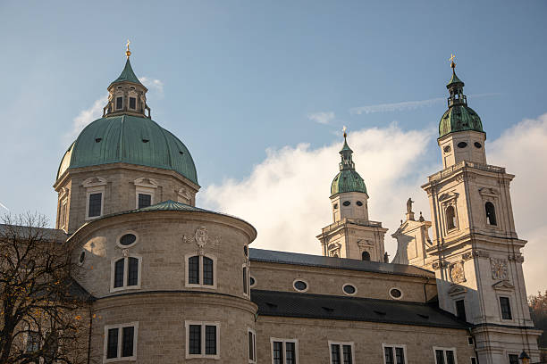 Low angle three-quarter side view of Salzburg Cathedral on blue sky day with low clouds.