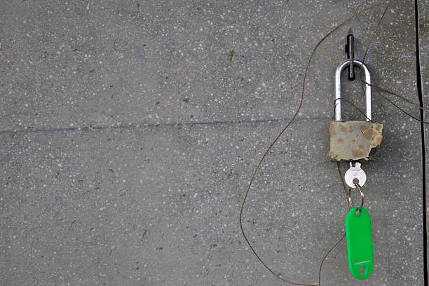A rusty padlock is secured by a wire with a key resting on a bright green tag against a gray, textured background.