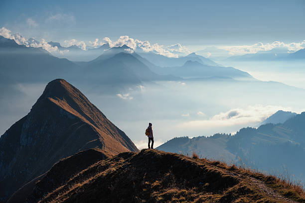 Woman with backpack standing on a mountain ridge above clouds