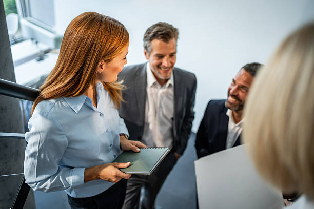 Diverse group of business people in professional attire meeting on office stairs, smiling and engaging in an informal discussion about strategy and teamwork