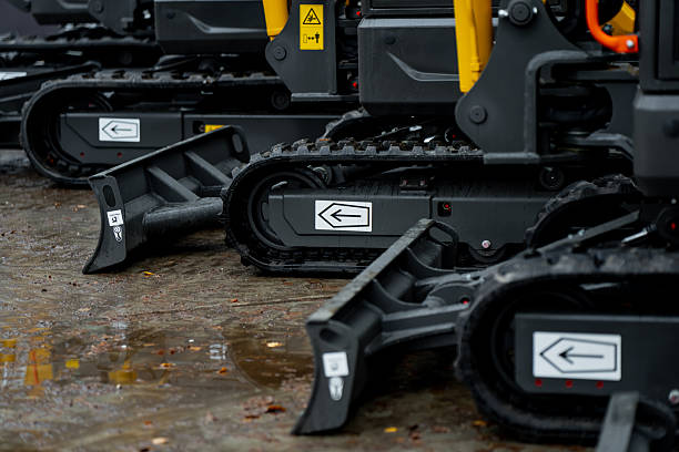 istock Row of compact excavators with rubber crawler tracks and hydraulic dozer blades aligned on wet construction surface showing traction and control systems 2245014949
