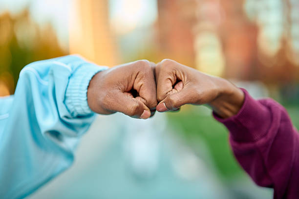 Two people's dark skin hands making a fist bump gesture outdoors, symbolizing friendship, partnership, support, and a successful collaboration after an exercise workout
