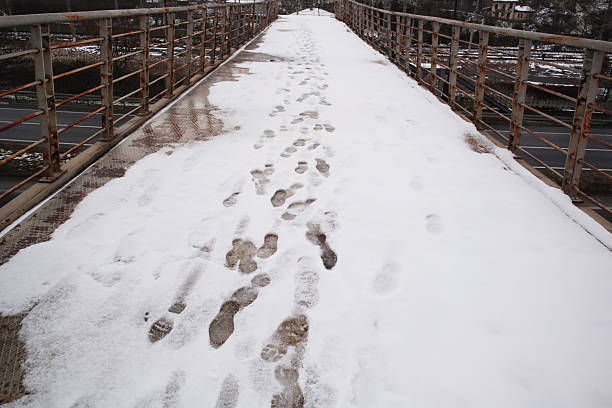 Close-up taken of metal pedestrian overpass with footprints in the snow