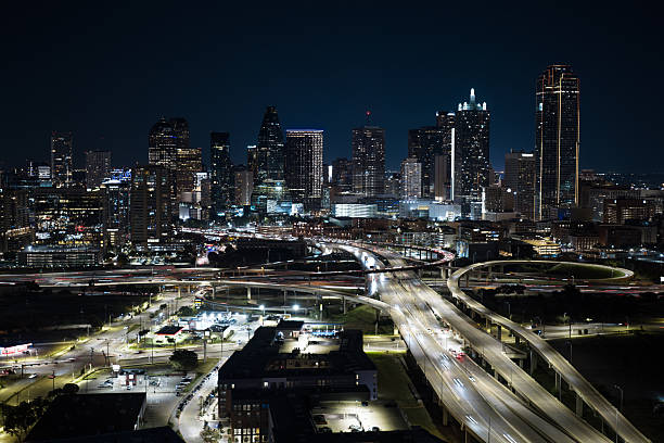 Aerial shot of traffic on the interchange of Texas State Highway Spur 366 and Interstate 35E on the edge of downtown Dallas, Texas at night with illuminated commercial and residential buildings beyond.