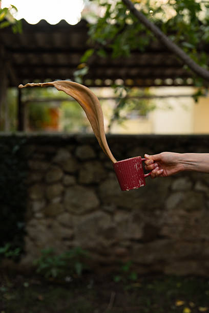 Close-up of a hand holding a cup of spilled coffee outdoors.