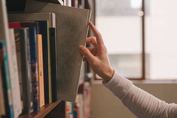 istock Hand picking book from library bookshelf for reading and education concept, symbolizing knowledge, education, learning, research, study, literature, academic resources in a quiet study environment 2245040268
