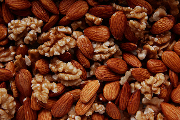 Blanched and raw almonds displayed on a wooden board next to a glass jar, showcasing different textures