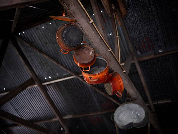 Rusty orange cooking pots suspended from wooden beam against corrugated metal ceiling in rustic setting