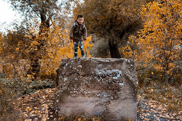 Young boy playing outdoors in fall nature, wearing a warm jacket and camouflage pants. Concept of exploring and adventure