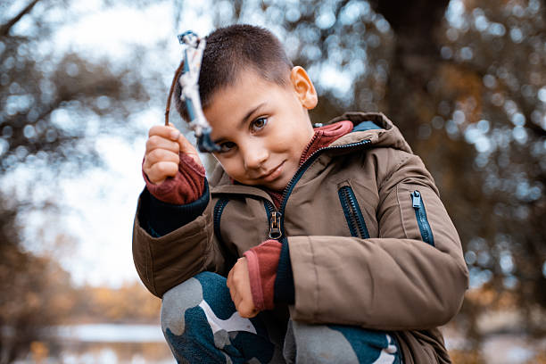 Young boy smiling, holding a handmade slingshot while enjoying outdoor play and childhood adventure in an autumn park