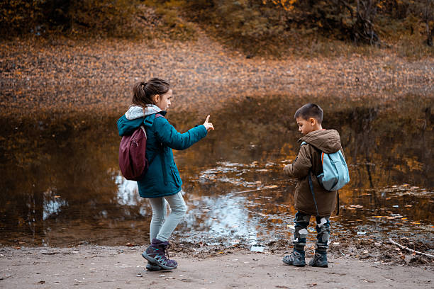Little girls watch their friend stir muesli in a lunchbox with a spoon while sitting on a stone fence by the sea. High quality photo