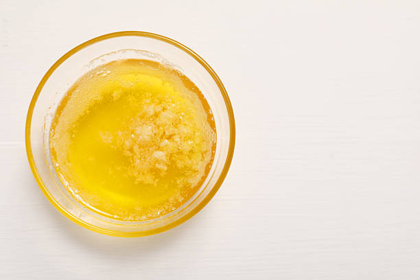 istock Melted butter in glass bowl on white wooden table, top view. Space for text 2245050314