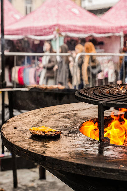 Vyborg, Russia – November 2025: A grilled burger patty topped with melting cheese cooks on an open flame during the Krendel Festival in Vyborg, Leningrad Region, Russia.