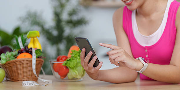 istock Digital Wellness. Woman using smartphone while surrounded by fresh vegetables, promoting healthy living. 2245060531