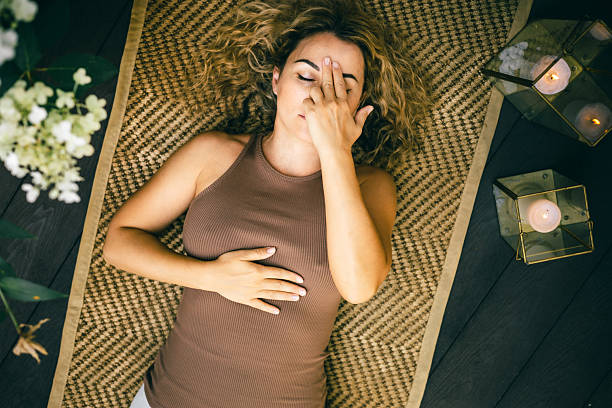 istock Woman practicing calming breathing technique while lying on mat with candles and flowers 2245061244