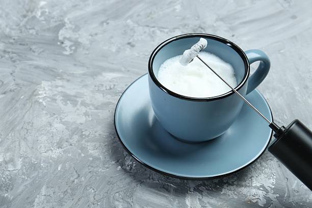 istock Mini mixer (milk frother) and whipped milk in cup on grey textured table, closeup. Space for text 2245070546