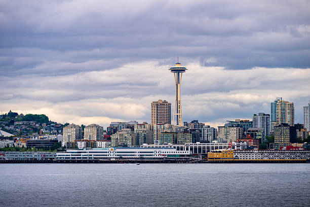 A dramatic view of downtown Seattle, Washington, captured from across Puget Sound under heavy clouds. The modern skyline features iconic skyscrapers like the Space Needle and waterfront buildings, illustrating the city’s urban density and architectural diversity.