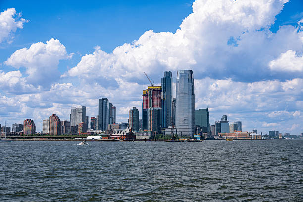 The modern skyline of Jersey City, New Jersey rises along the Hudson River, with glass skyscrapers and ongoing construction framed by dramatic summer clouds. A vibrant and growing financial hub opposite Lower Manhattan.