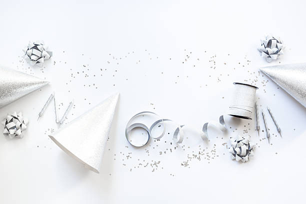 Silver party decoration - streamers with confetti and cones on white background, top view.