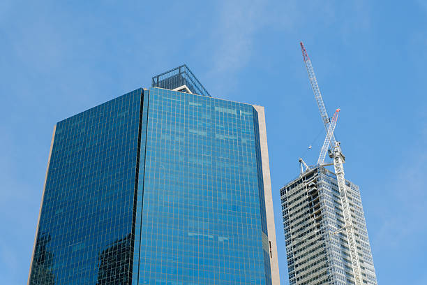 Two tall city office buildings with one still under construction. Crane is attached to the side.