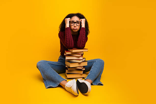 istock Young mixed race female student with stylish glasses yellow background with a tall stack of book expressing joy and learning in casual fashion 2245090438