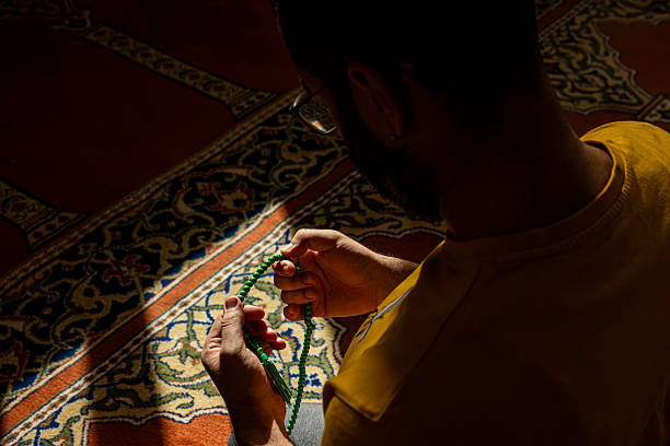 On a prayer mat at home, an Indonesian man raises open palms in dua to Allah, seeking forgiveness and expressing gratitude, after performing shalat during Ramadan