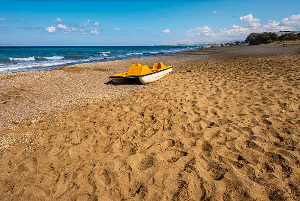 Yellow pedal boat on empty beach in summer sunny day. Amoudara, Crete, Greece.