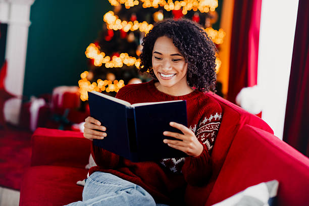 istock Cozy reader woman in red sweater on a red sofa reading a book beside a bright christmas tree at home during christmas season 2245098255