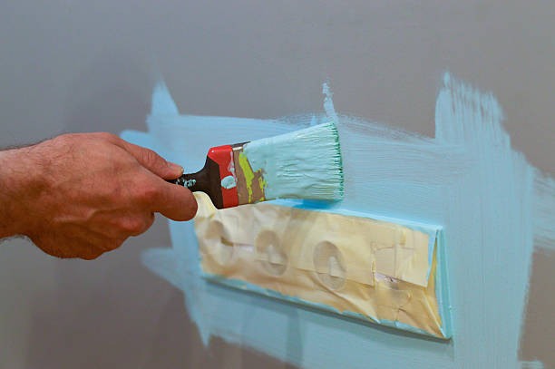 istock Using a brush to paint around an electrical socket on the wall, with masking tape applied for protection, as a DIY interior repair, aiming for precise results and safety. 2245099673