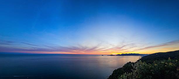 Panoramic view of a serene ocean at sunset with vibrant sky colors and distant islands.