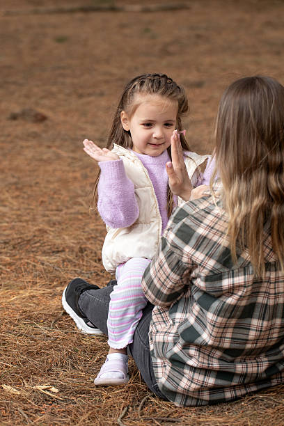 istock Mother and daughter playing patty-cake together while sitting in a pine forest. 2245104563