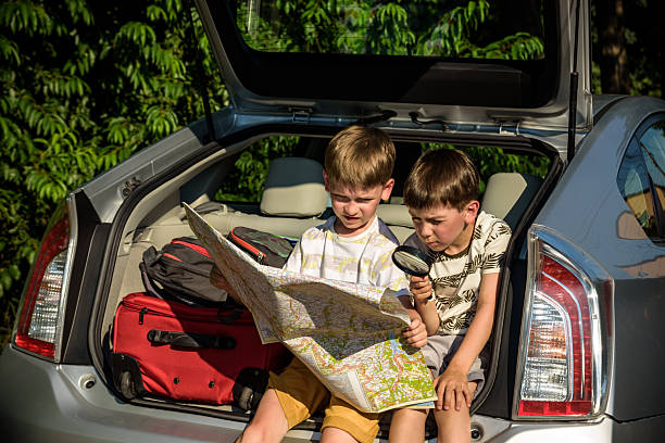 istock Two cute boys sitting in a car trunk before going on vacations with their parents. Kids sitting in a car examining a map. Summer break at school. Family travel by car 2245104671