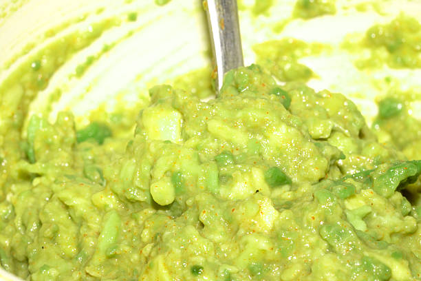 A close-up view of a creamy mound of mashed avocado being gently pressed onto a golden slice of fresh bread